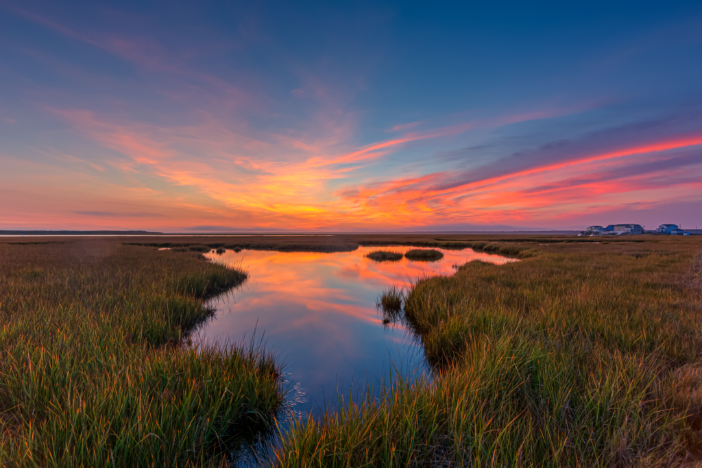 14mm wide angle photo made after sunset overlooking Cedar Run Dock Road salt marsh. Deep blues fill a sky alight with sweeping pastel clouds reflected in a marsh pool.