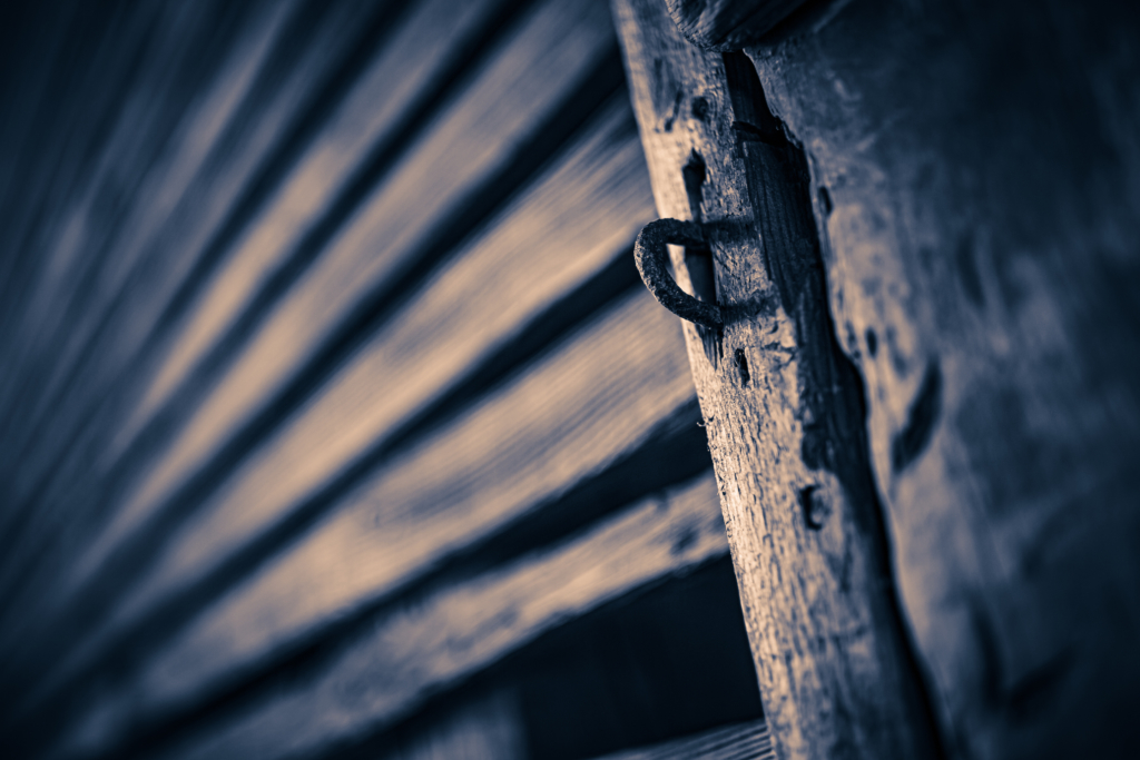 35mm sepia photograph of an old wooden structure marked by leading lines, knotted wood, and a rusted iron locking loop. 