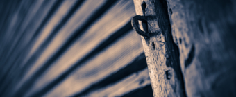 35mm sepia photograph of an old wooden structure marked by leading lines, knotted wood, and a rusted iron locking loop.