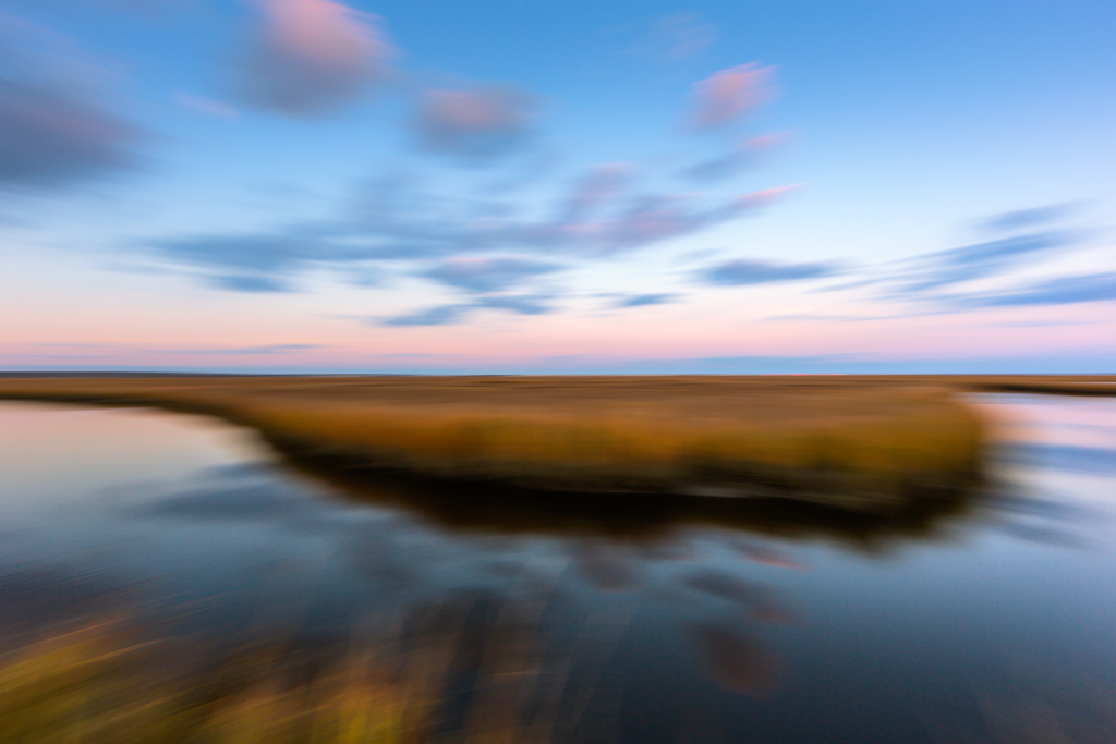 14mm blue hour photo purposefully out of focus capturing passing clouds and salt marsh with intentional camera side motion blur.