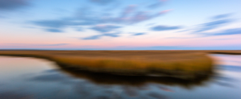 14mm blue hour photo purposefully out of focus capturing passing clouds and salt marsh with intentional camera side motion blur.