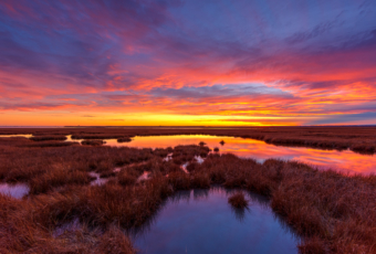 14mm wide angle HDR sunset photo of a winter sky glowing with deep pastel colored clouds reflected above Cedar Run Dock Road salt marsh.