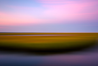 35mm panning shot photo of a New Jersey salt marsh at sunset. Late summer green marsh gives way to orange and yellow hues in a landscape picture blurred by motion.