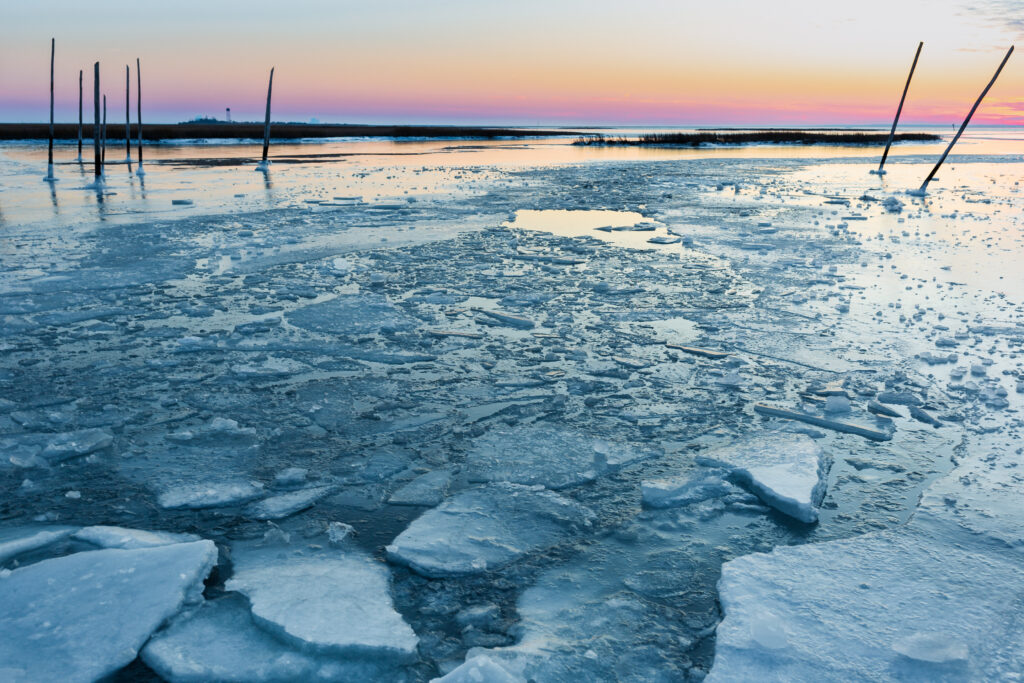 Ice chunks scatter the surface of a frozen bay with derelict dock posts photographed at 35mm. 