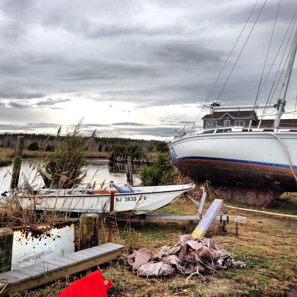 A large sailboat and a smaller boat sit ashore beside damaged docks and marsh grass.