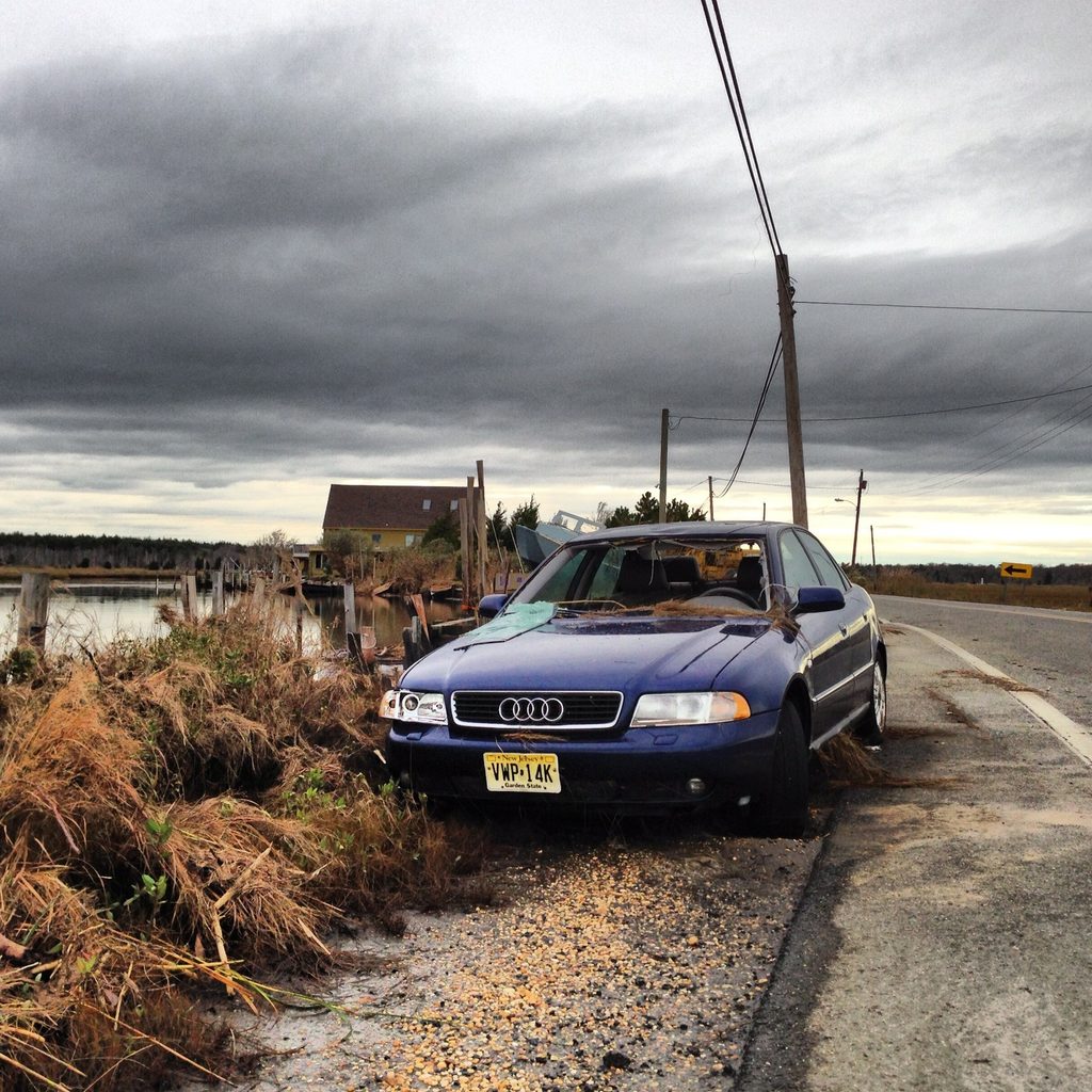 A blue Audi stands beside a visibly bent utility pole at the edge of a road.
