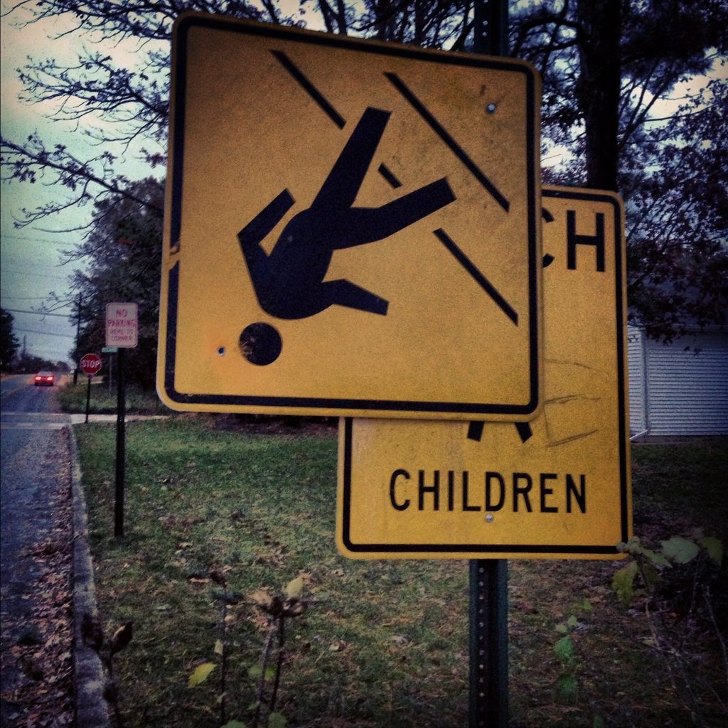 A yellow school-crossing road sign appears upside down beside a street.