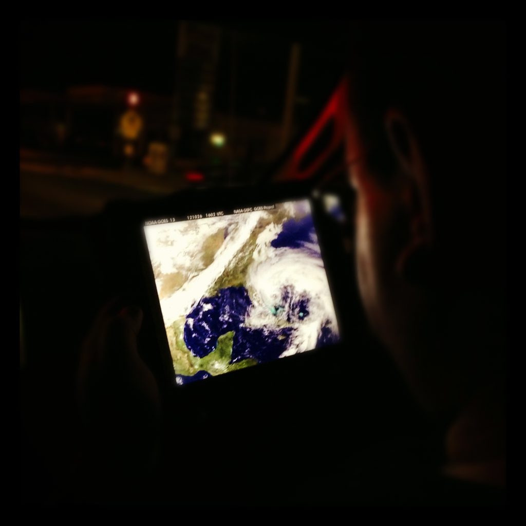 An iPad displaying NOAA GOES-13 satellite imagery is held inside a vehicle at night.