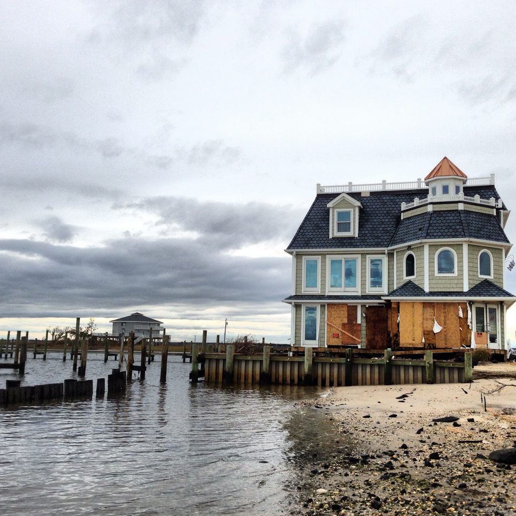 A multistory house beside a water-covered shoreline under heavy gray clouds.